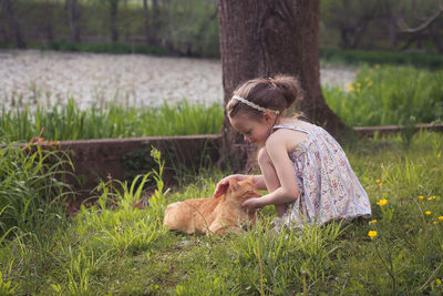 Side view of girl with cat crouching on grassy field at park