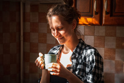 Young woman hold and enjoy aromatic cup of coffee in morning sunlight at home