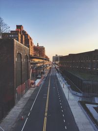 Road amidst buildings in city against clear sky during sunset