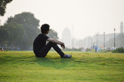 Full length of man sitting grassy field at park during foggy weather