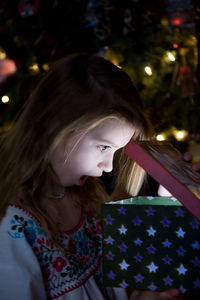 Surprised girl looking into christmas present at night