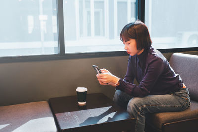 Young man using mobile phone while sitting on window