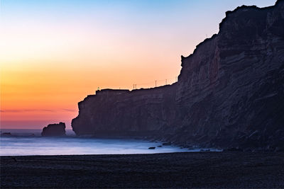 Rock formations on beach against sky during sunset