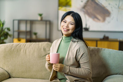 Young woman using mobile phone while sitting on sofa at home