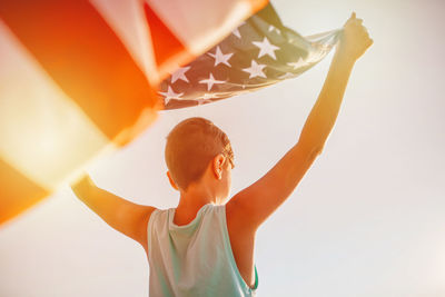 Rear view of man holding american flag against sky