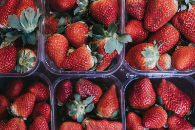 Top view of fresh strawberries on sale, portioned in plastic boxes, on top of a wooden table.