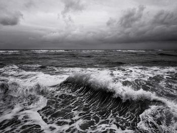 Scenic view of waves splashing in sea against cloudy sky