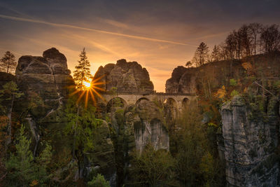 Trees and rocks against sky during sunset