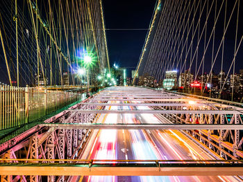 Light trails on road amidst illuminated buildings against sky at night