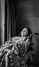 Woman looking away while sitting in a wheelchair near window at home