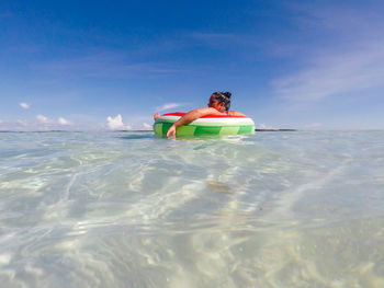 Young woman floating on inflatable ring in sea against blue sky