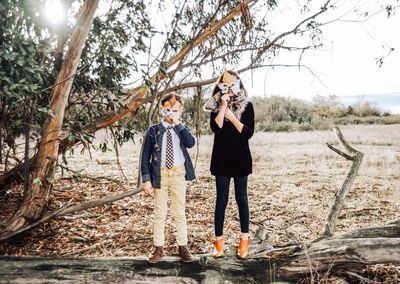 Portrait of siblings holding maple leaves over face while standing in park during autumn