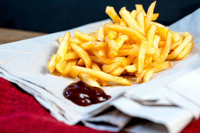 Close-up of fresh french fries served with ketchup on napkin