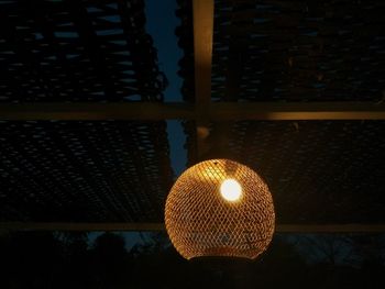 Low angle view of illuminated light bulb hanging against window