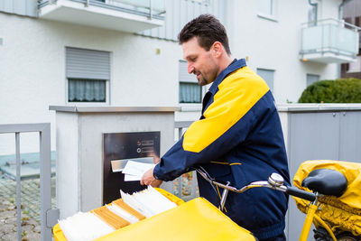 Side view of postal worker inserting letters in mailbox