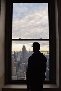 Rear view of man looking at empire state building amidst city through window