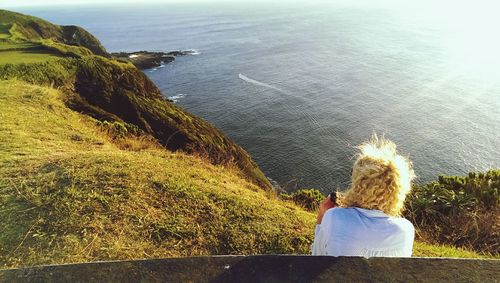 Rear view of man sitting on rock by sea