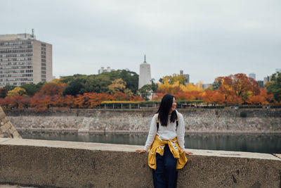 Rear view of woman standing by buildings in city against sky