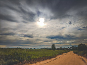 Dirt road amidst field against sky