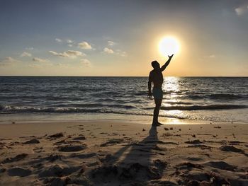 Silhouette man standing on beach against sky during sunset