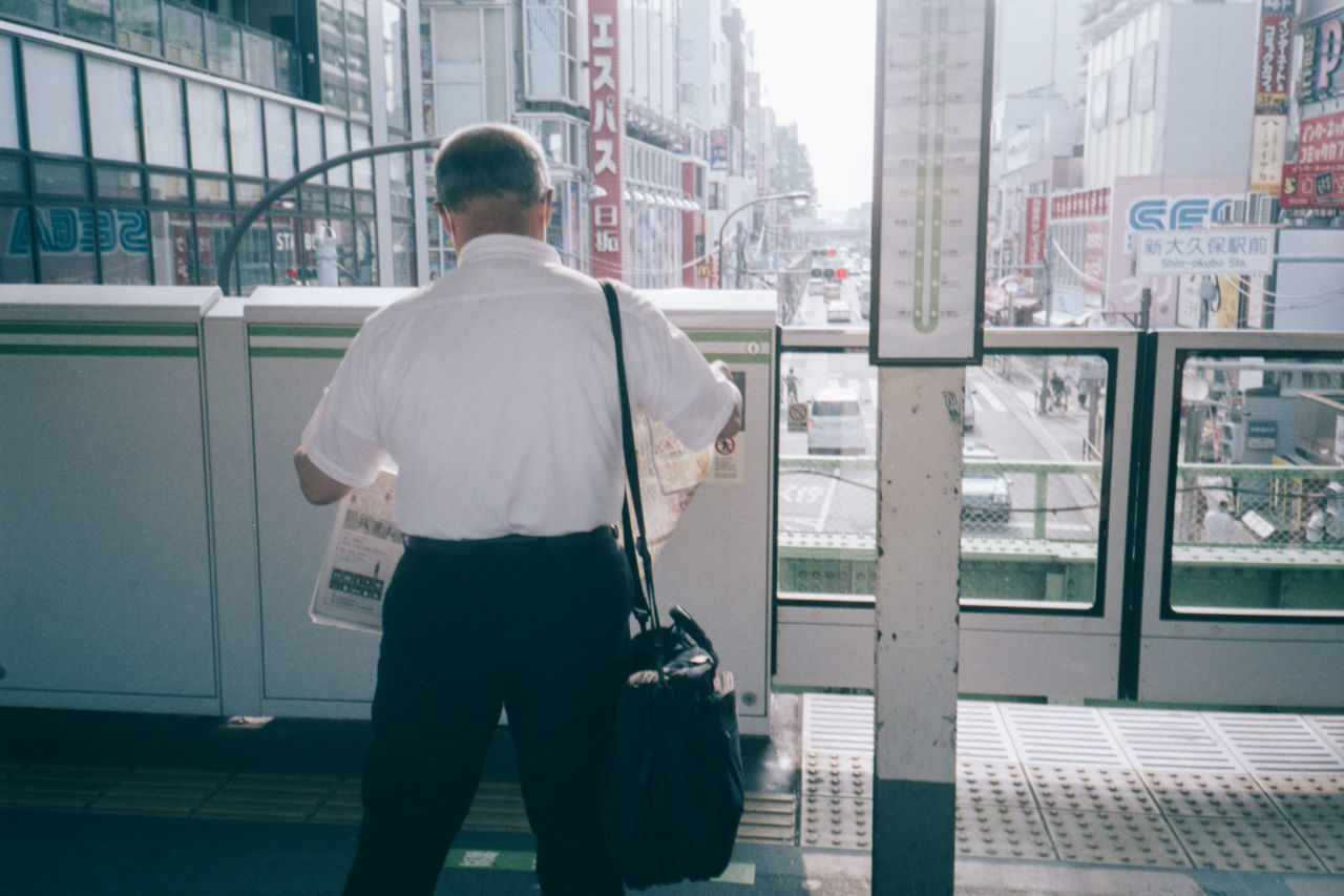 rear view, architecture, one person, city, men, built structure, adult, building exterior, standing, day, businessman, street, city life, business, office building exterior, luggage and bags, building, travel, office, road, transportation, outdoors, full length, three quarter length