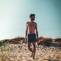 Full length of shirtless man walking at beach against clear sky