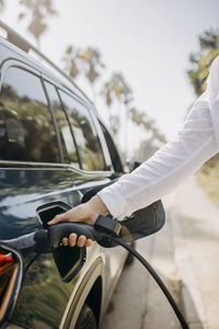 Hand of man holding charging plug of electric car at roadside