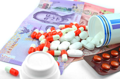 Close-up of medicines and paper currency over white background