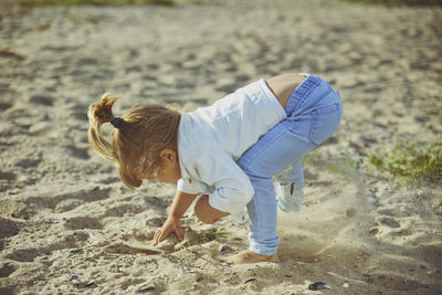 Charming child digs a hole on the beach like a dog