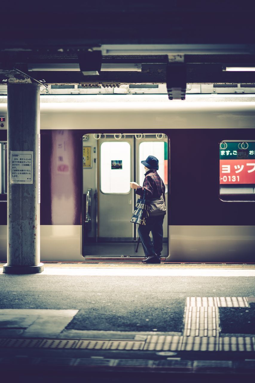 FULL LENGTH REAR VIEW OF MAN WALKING ON ILLUMINATED RAILROAD STATION