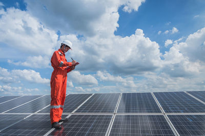 Engineer standing on solar panel against cloudy sky