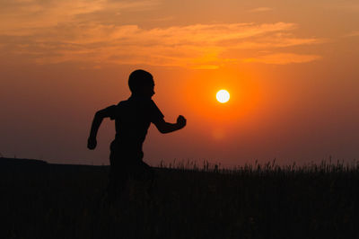 Silhouette boy running on field against orange sky during sunset