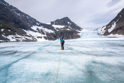 Hikers on frozen lake amidst mountains