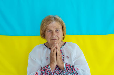 Senior woman with hands clasped against ukrainian flag