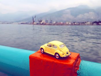 Close-up of yellow toy car by sea against sky