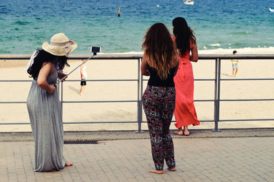 Rear view of women standing by railing against sea