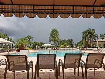 Chairs and table by swimming pool against sky