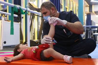 A male physical therapist treats a child in a physical therapy center, physiotherapy. war casualties