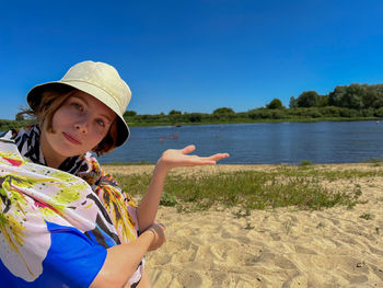 Portrait of young woman standing at beach against sky