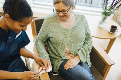 Smiling senior woman looking at young female caretaker filing her nails in retirement home