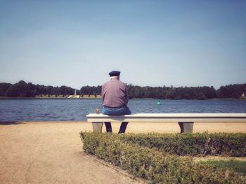 Rear view of man sitting by lake against sky