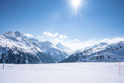 Scenic view of shining sun through blue sky over snow covered mountains