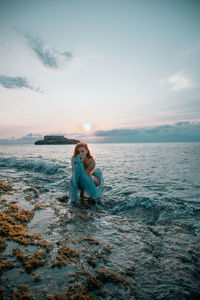 Woman in sea against sky during sunset