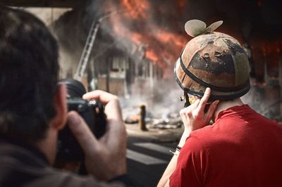 Rear view of photographer and journalist watching building set on fire 