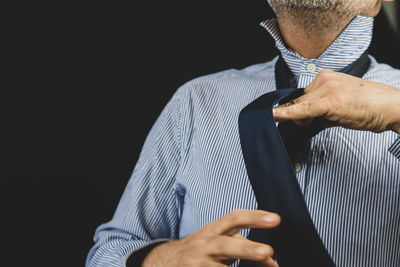 Midsection of man wearing tie against black background