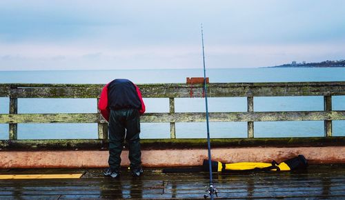 Rear view of man bending on pier over sea against sky