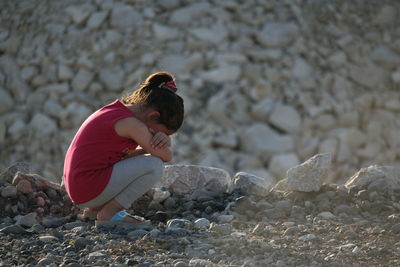 Side view of girl crouching on pebbles at beach