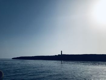 Silhouette lighthouse by sea against clear sky