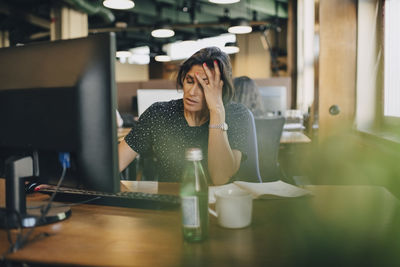 Tired businesswoman with head in hand sitting at computer desk in office