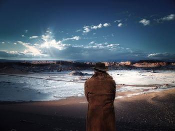 Rear view of man looking at landscape against sky during winter